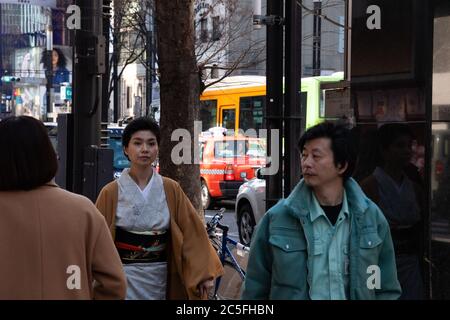 Des gens qui marchent sur un trottoir, une femme élégante portant un kimono de luxe traditionnel dans le quartier de Ginza. Trafic en arrière-plan. Tokyo, Japon. Banque D'Images