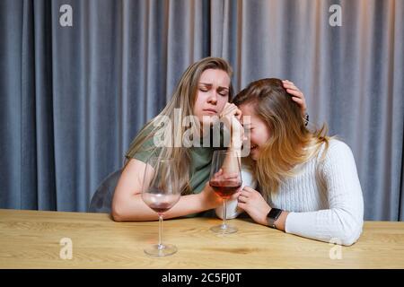 Une femme console une triste amie dépressive qui a besoin d'aide. Dépression avec alcool concept. Bouleversé jeune fille avec visage malheureux tenant un verre de vin lo Banque D'Images