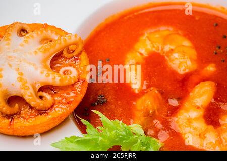 Bol De Soupe De Tomates Aux Crevettes Avec Une Petite Pieuvre Cuite Sur Une  Tranche D'orange Sur Un Bac En Bois Noir