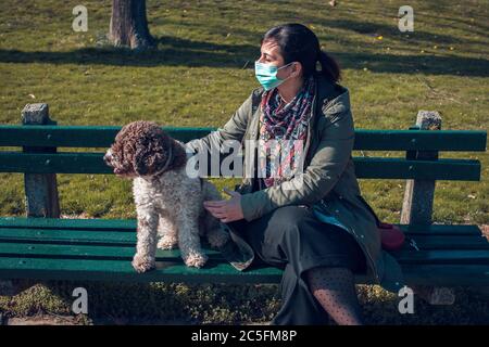 femme avec masque de visage assis sur le banc avec son chien Banque D'Images