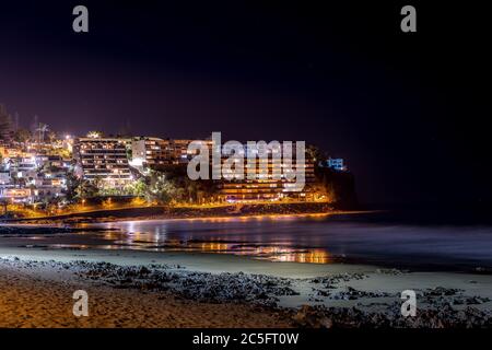 Vue nocturne de la ville sur une falaise de roche capturée en soirée avec reflet des ombres sur la surface de l'océan et autres reflets de la lumière de la rue sur la surface. Banque D'Images