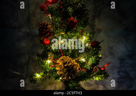 petit arbre décoré de noël avec des décorations rouges et dorées allume lentement une chaîne légère enroulée autour d'un arbre de lumières de couleur jaune Banque D'Images