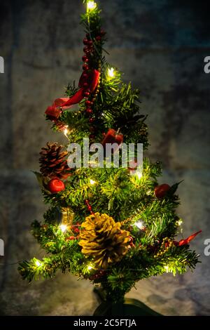 petit arbre décoré de noël avec des décorations rouges et dorées allume lentement une chaîne légère enroulée autour d'un arbre de lumières de couleur jaune Banque D'Images