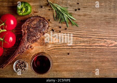 Griller une côte de bœuf vieilli avec des légumes et un verre de vin rouge sur fond de bois Banque D'Images