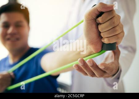 Gros plan de la main patient faisant de l'exercice avec un bracelet d'exercice flexible et une main de thérapeute physique pour aider dans la salle de clinique. Banque D'Images