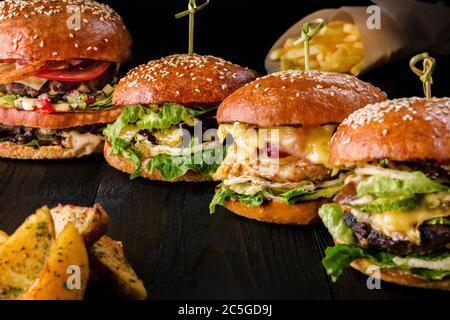 Quatre hamburgers faits maison sur une table en bois. Petits pains aux graines de sésame, hamburgers de bœuf et divers ingrédients. Banque D'Images