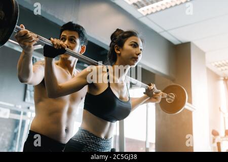 Entraîneur personnel aidant les femmes et de manipuler les cloches lourdes deux mains haut un épaule dans la salle de gym. Banque D'Images