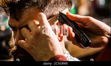 Concept de coupe de cheveux. Homme visitant le coiffeur dans le salon de coiffure. Le coiffeur fonctionne avec une tondeuse à cheveux. Client Hipster se couper la coiffure. Mains de coiffeur avec cheveux Banque D'Images