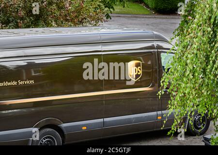 Un camion de service de messagerie UPS de couleur marron s'est arrêté dans une rue alors que le conducteur déroute un colis. Banque D'Images
