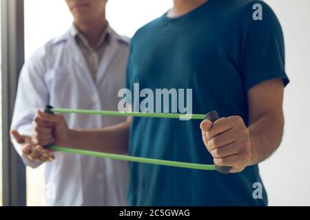 Patient faisant de l'exercice d'étirement avec un bracelet d'exercice flexible et une main de thérapeute physique pour aider dans la salle de clinique. Banque D'Images