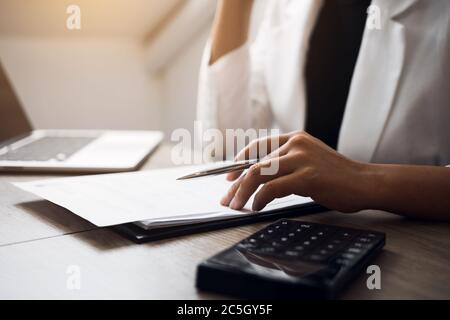 Des femmes sont assises à analyser le plan de l'état financier de l'entreprise à l'aide d'une calculatrice sur son bureau. Banque D'Images