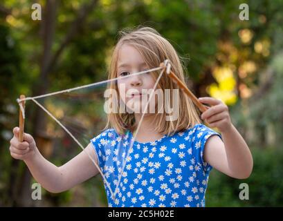 Jeune fille dans une robe bleue et blanche soufflant de grandes bulles avec une corde dans une cour arrière Banque D'Images