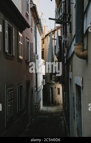 Ruelle romantique de la vieille ville côtière historique Piran en Slovénie bordée de maisons avec des volets fermés et des vêtements de séchage suspendus Banque D'Images