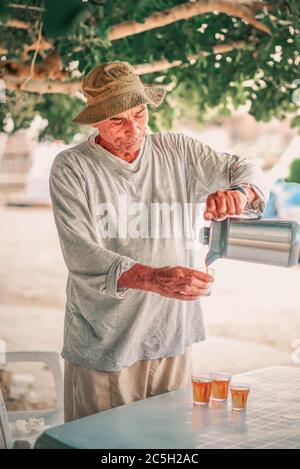 Homme mature et hospitalier versant du thé chaud de la théière dans un petit verre dans un jardin. Banque D'Images