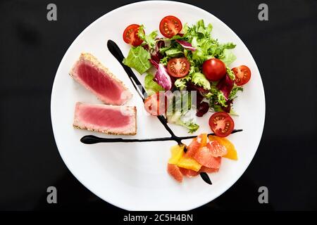 Filet de poulet moyen-rare avec salade de tomates. Plat sur fond noir. Banque D'Images