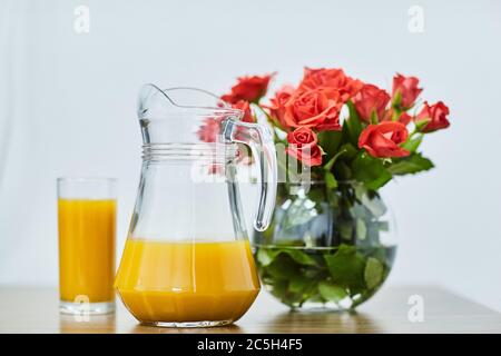 Un verre de jus d'orange avec un pichet. Bouquet de roses. Fleurs. Banque D'Images