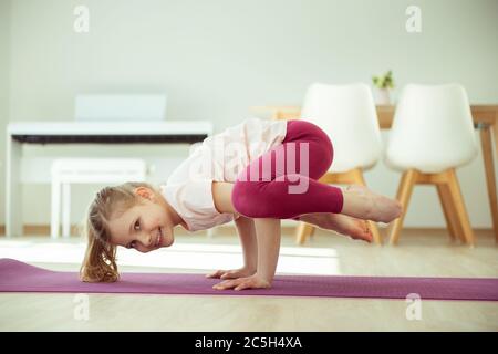 Jolie fille d'enfant heureux ayant plaisir à faire des exercices de yoga à la maison pendant la quarantaine de coronavirus Banque D'Images