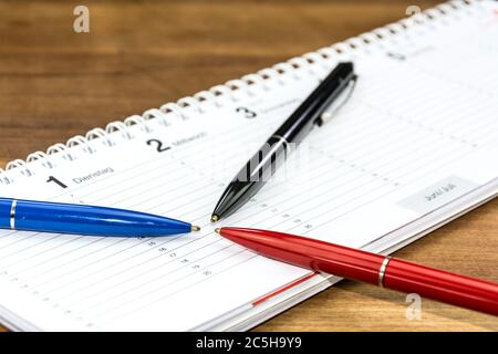 Stylos posés sur un horaire et poting vers une date et une heure spécifiques (avec légendes des jours de la semaine en allemand) Banque D'Images