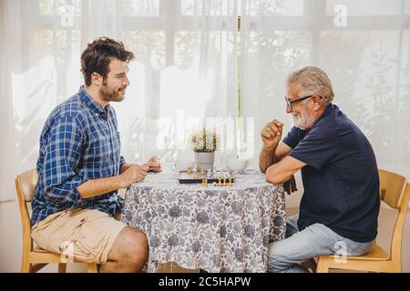Smart Elder jouant jeu de plateau d'échecs à la maison avec un jeune homme pour rester en bonne santé du cerveau Banque D'Images