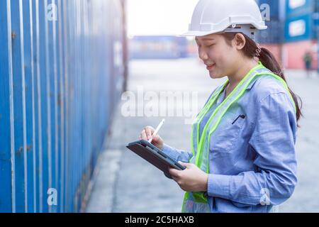 Femme employée heureuse de travailler dans l'expédition logistique de la zone de chargement utiliser la technologie sans fil de tablette pour vérifier les détails douaniers de l'importation exportation conta Banque D'Images