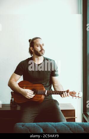 Homme jouant de la guitare regardant loin manquant quelqu'un seul à la maison vintage couleur ton vertical tourné. Banque D'Images