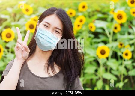 Mignon fille adolescent Happy ware masque pour protéger le coronavirus (Covid-19) ou pollution de l'air ou allergie de pollen de fleur sur fond de parc de tournesol Banque D'Images