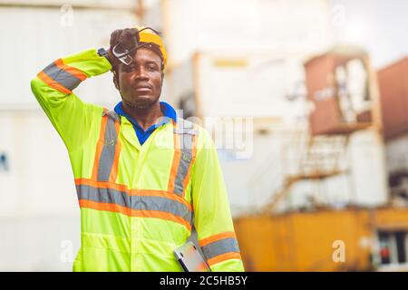 Travailleur de stress fatigué sueur par temps chaud en été travaillant dans le port marchandises fret maritime logistique terrain, Black African race People. Banque D'Images