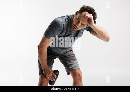 Image d'un jeune homme fatigué utilisant des écouteurs et tenant une bouteille d'eau tout en s'faisant de l'activité sur fond blanc Banque D'Images