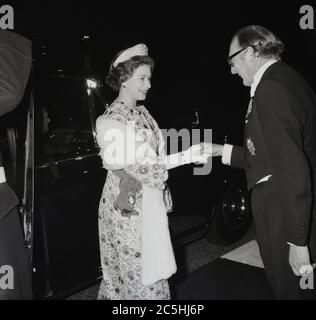 1973, historique, le soir et à l'extérieur de son véhicule, Rolls Royce, la reine du Royaume-Uni, sa Majesté la reine Elizabeth II, étant officiellement accueillie par un membre du Royal Naval College, Greenwich, Londres, Angleterre, Royaume-Uni. Banque D'Images