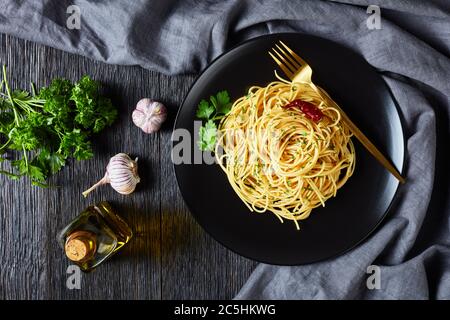 Pâtes Alla colatura di alici, spaghetti à la sauce anchois, piment, ail et persil sur une assiette noire avec fourchette dorée sur un tabl en bois foncé Banque D'Images