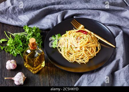Pâtes Alla colatura di alici, spaghetti à la sauce anchois, piment, ail et persil sur une assiette noire avec fourchette dorée sur un tabl en bois foncé Banque D'Images