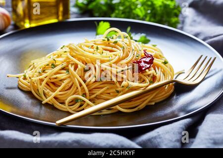 Spaghetti Alla colatura di alici, spaghetti à la sauce anchois, piment, ail et persil sur une assiette noire avec fourchette dorée sur une face sombre Banque D'Images
