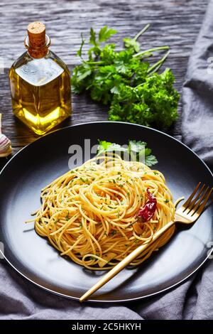 Pâtes Alla colatura di alici, spaghetti à la sauce anchois, piment, ail et persil sur une assiette noire avec fourchette dorée sur un tabl en bois foncé Banque D'Images