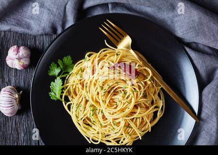 Pâtes Alla colatura di alici, spaghetti à la sauce anchois, piment, ail et persil sur une assiette noire avec fourchette dorée sur un tabl en bois foncé Banque D'Images