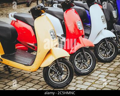 Les motos électriques de différentes couleurs se trouvent en rangée sur une dalle de pavage. Banque D'Images