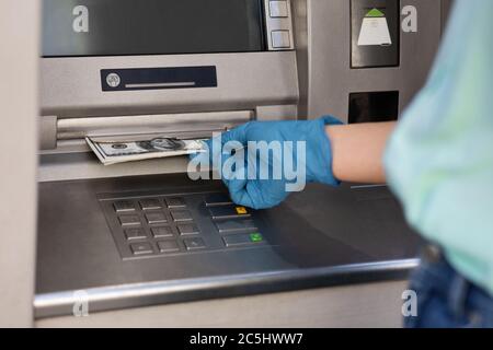 Main féminine dans un gant médical de protection prenant l'argent de la machine ATM Banque D'Images