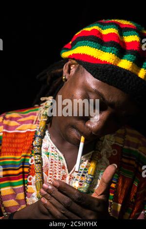 Visage du jeune homme rastafarien africain éclairant la cigarette à l'extérieur la nuit Banque D'Images