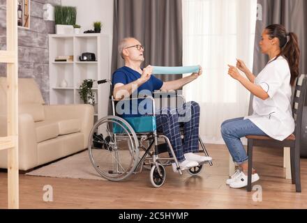 Homme âgé avec une incapacité en fauteuil roulant effectuant un exercice de récupération avec une bande de résistance. Personne handicapée handicapée avec travailleur social dans le soutien de la thérapie de soutien de la physiothérapie système de santé de soins infirmiers maison de retraite Banque D'Images