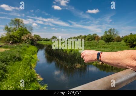 Femme aux bras pliés vue sur un petit pont de rivière dans la campagne anglaise. Elle porte une montre de fitness et ses bras sont bronzés. Banque D'Images