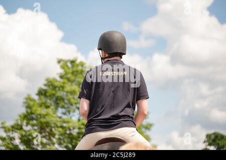 Jeune cavalier équestre mâle vu avec un casque standard de l'émission de son cheval pendant une journée ensoleillée. Banque D'Images