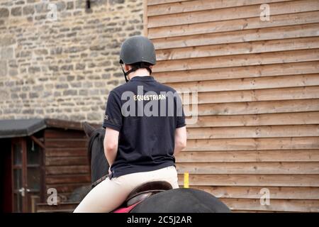 Jeune cavalier équestre mâle vu avec un casque standard de l'émission de son cheval pendant une journée ensoleillée. Banque D'Images