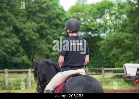 Jeune cavalier équestre mâle vu avec un casque standard de l'émission de son cheval pendant une journée ensoleillée. Banque D'Images