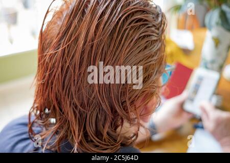 Très peu profonde de mise au point de certains des cheveux récemment teints vus sur une femme d'âge moyen à la maison. Elle est vue utiliser un téléphone portable pour vérifier ses factures. Banque D'Images