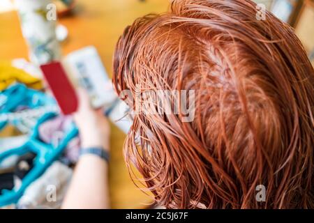 Très peu profonde de mise au point de certains des cheveux récemment teints vus sur une femme d'âge moyen à la maison. Elle est vue utiliser un téléphone portable pour vérifier ses factures. Banque D'Images