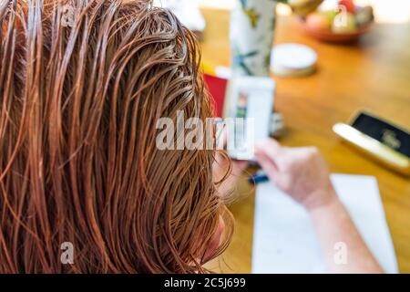 Très peu profonde de mise au point de certains des cheveux récemment teints vus sur une femme d'âge moyen à la maison. Elle est vue utiliser un téléphone portable pour vérifier ses factures. Banque D'Images