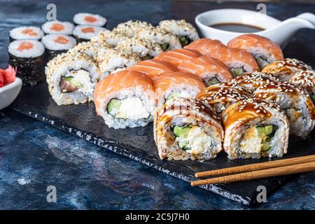 Une boîte de sushi Nigiri, Uramaki California, Philadelphie, sur une assiette en pierre noire. Menu de sushis dans un coffret de transport blanc sur fond de bois. Foregroun Banque D'Images