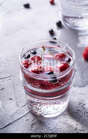 Eau fraîche et gazeuse buvez avec des baies de cerisier, framboise et cassis dans deux verre transparent sur fond de béton de pierre, l'été régime beverag Banque D'Images