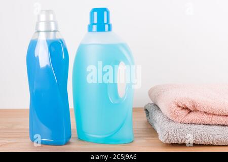 Bouteilles de détergent et assouplissant avec des serviettes propres sur une table en bois. Récipients de produits de nettoyage. Détergent liquide et conditionneur. Blanchisserie Banque D'Images