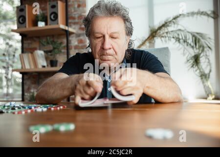 Passionnant. Joyeux homme mature jouant des cartes et buvant du vin avec des amis. Il a l'air ravi, enthousiaste. Homme caucasien jouant à la maison. Émotions sincères, bien-être, expression faciale concept. Bon vieux. Banque D'Images