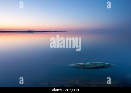 Paysage minimaliste tranquille avec roche dans l'eau calme du lac avec surface lisse avec horizon avec ciel bleu clair au crépuscule, simple beau calme Banque D'Images